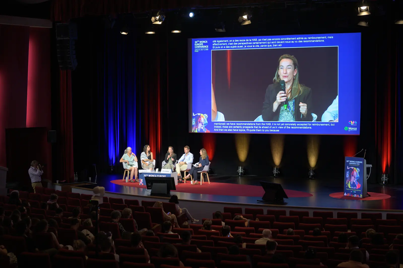 Vue de salle pendant une conférence, intervenants sur scène et écran géant
